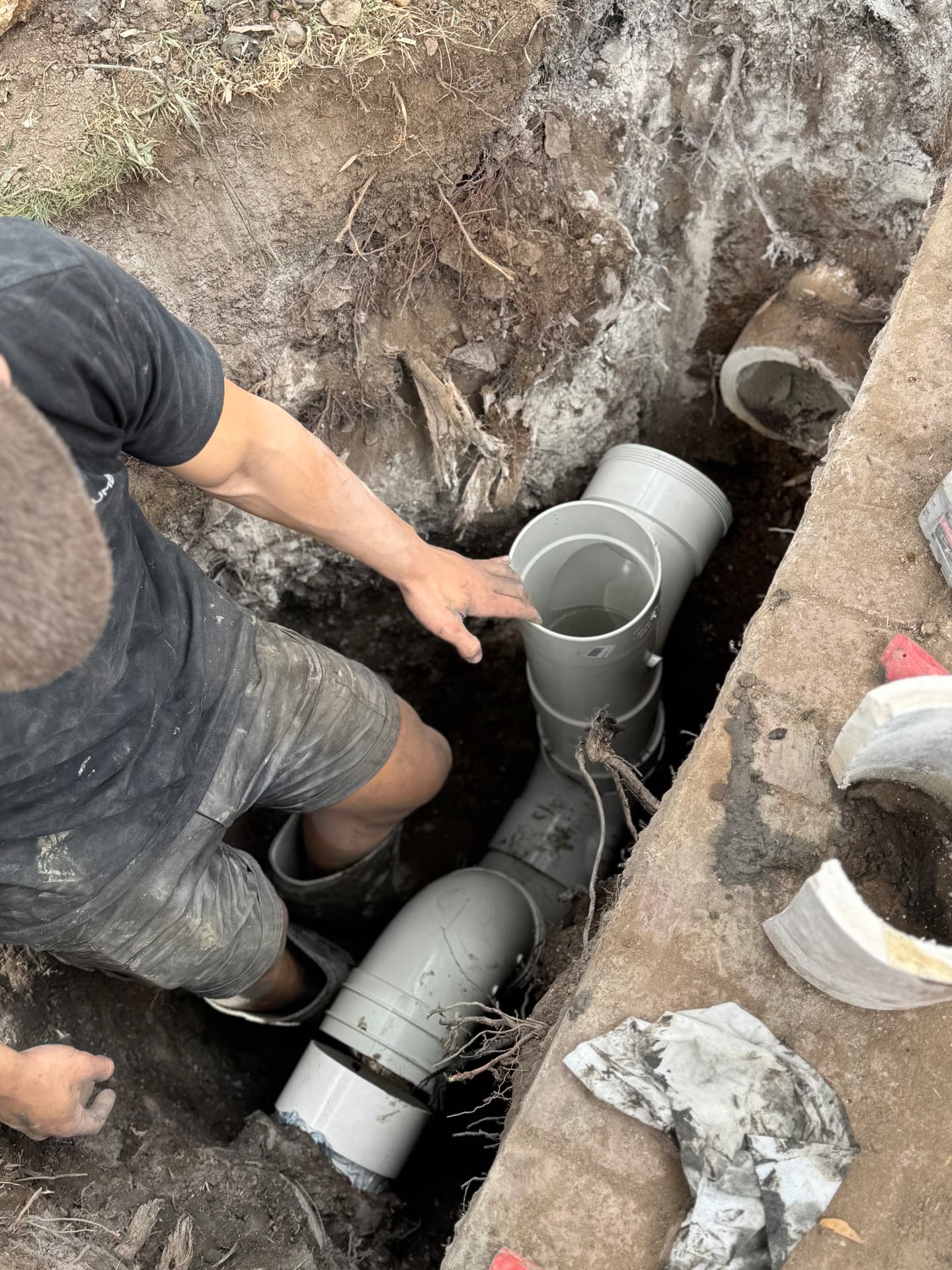 One Plumb fitting new PVC drainage pipework in an open trench